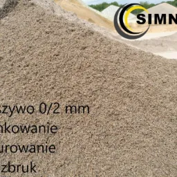 Góra kruszywa o granulacji 0/2 mm, przeznaczona do tynkowania, murowania i pozbruku, z widocznym logo firmy SIMNAT w prawym górnym rogu i innymi hałdami kruszyw w tle.