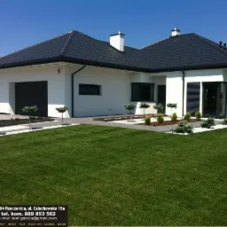 Nowoczesny dom z czarną stolarką okienną i roletami zewnętrznymi. Biała elewacja, ciemny dach i zadbany trawnik. Widoczne okna i rolety.