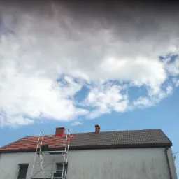 Dom z częściowo zdjętym starym dachem, widoczne przygotowanie pod nowe pokrycie i rusztowanie na tle pochmurnego nieba.