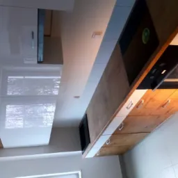 Nowoczesna kuchnia z drewnianymi frontami szafek i białymi, lakierowanymi górnymi szafkami, widoczny piekarnik i płyta grzewcza.