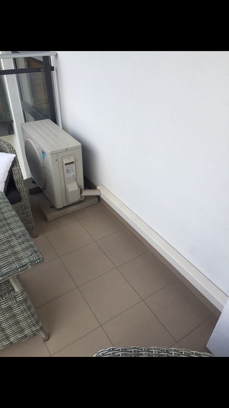 Zewnętrzna jednostka klimatyzacji Daikin zainstalowana na balkonie, widoczny fragment mebli ogrodowych z rattanu.