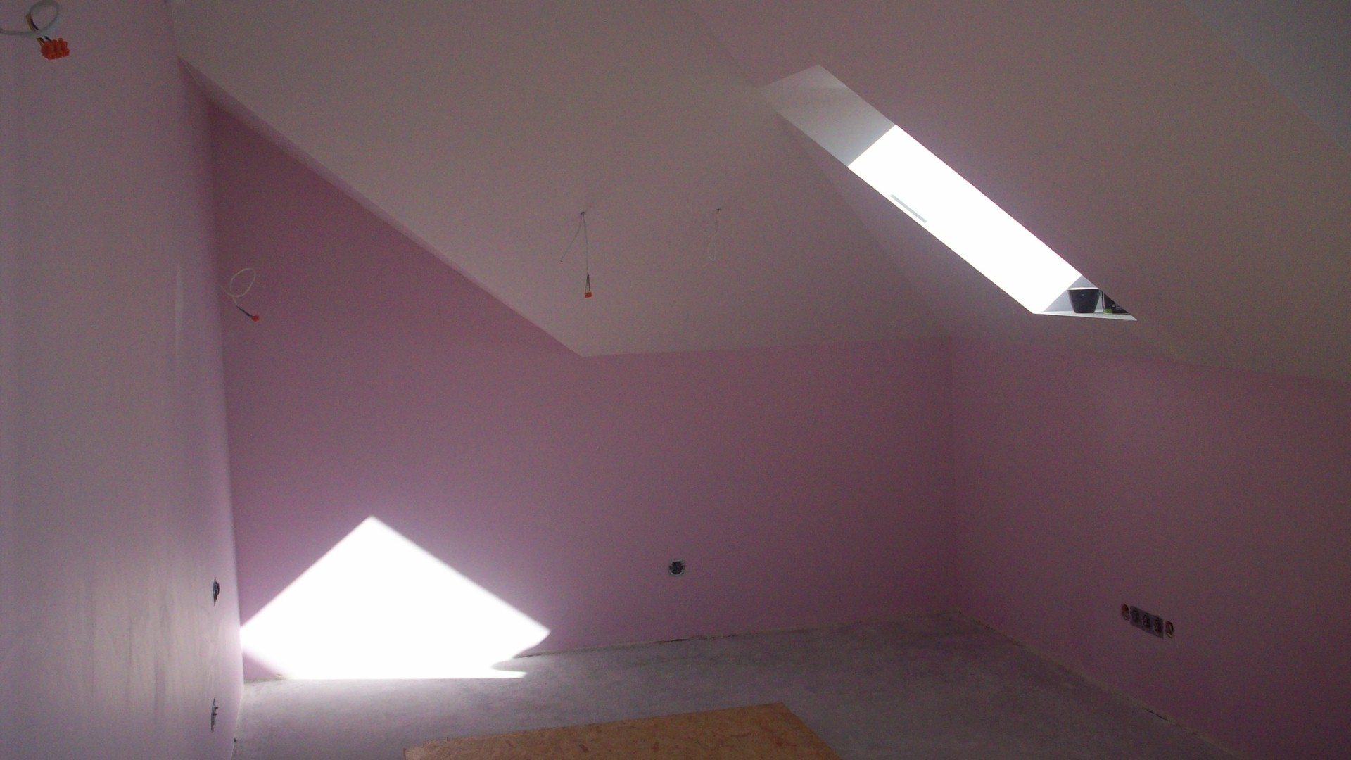 Poddasze po malowaniu na różowo, widoczne okno dachowe z doniczką, wystające kable i gniazdka elektryczne.
