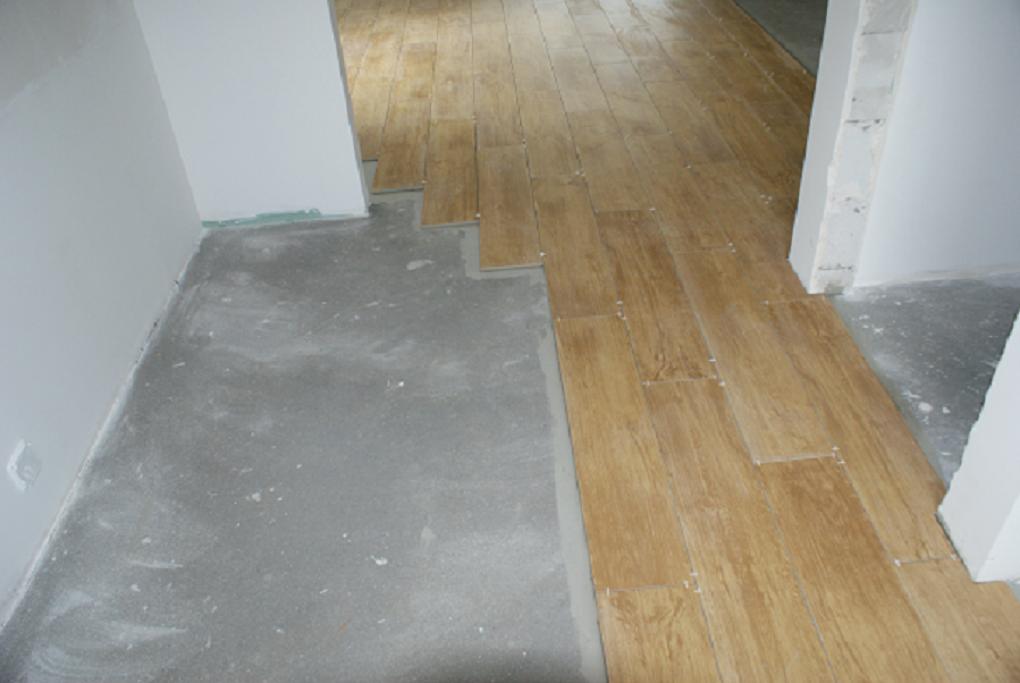 Układanie podłogi z płytek imitujących drewno, widoczny etap kafelkowania z niezakończoną powierzchnią i surowym podłożem.