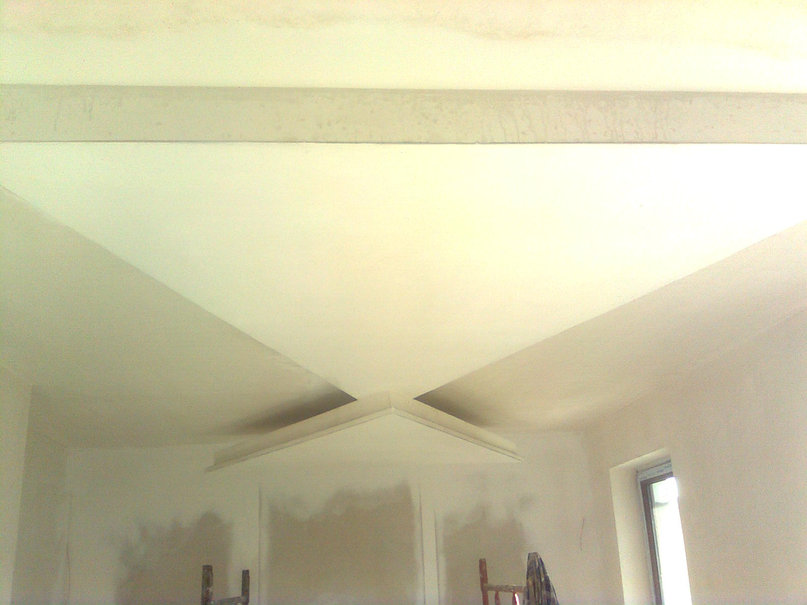 Wykończone poddasze z widoczną konstrukcją sufitu podwieszanego, ściany przygotowane do malowania, fragment okna i drabiny w tle.