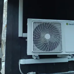 Zewnętrzna jednostka klimatyzacji marki Beretta zamontowana na ciemnej, drewnianej ścianie budynku. Widoczne przewody i elementy montażowe.