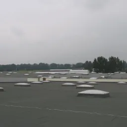 Rozległy, płaski dach przemysłowy pokryty papą z licznymi świetlikami kopułowymi, widok z góry w pochmurny dzień.