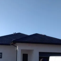 Nowoczesny dom jednorodzinny z ciemną dachówką modułową i orynnowaniem, zaparkowany biały bus w tle.