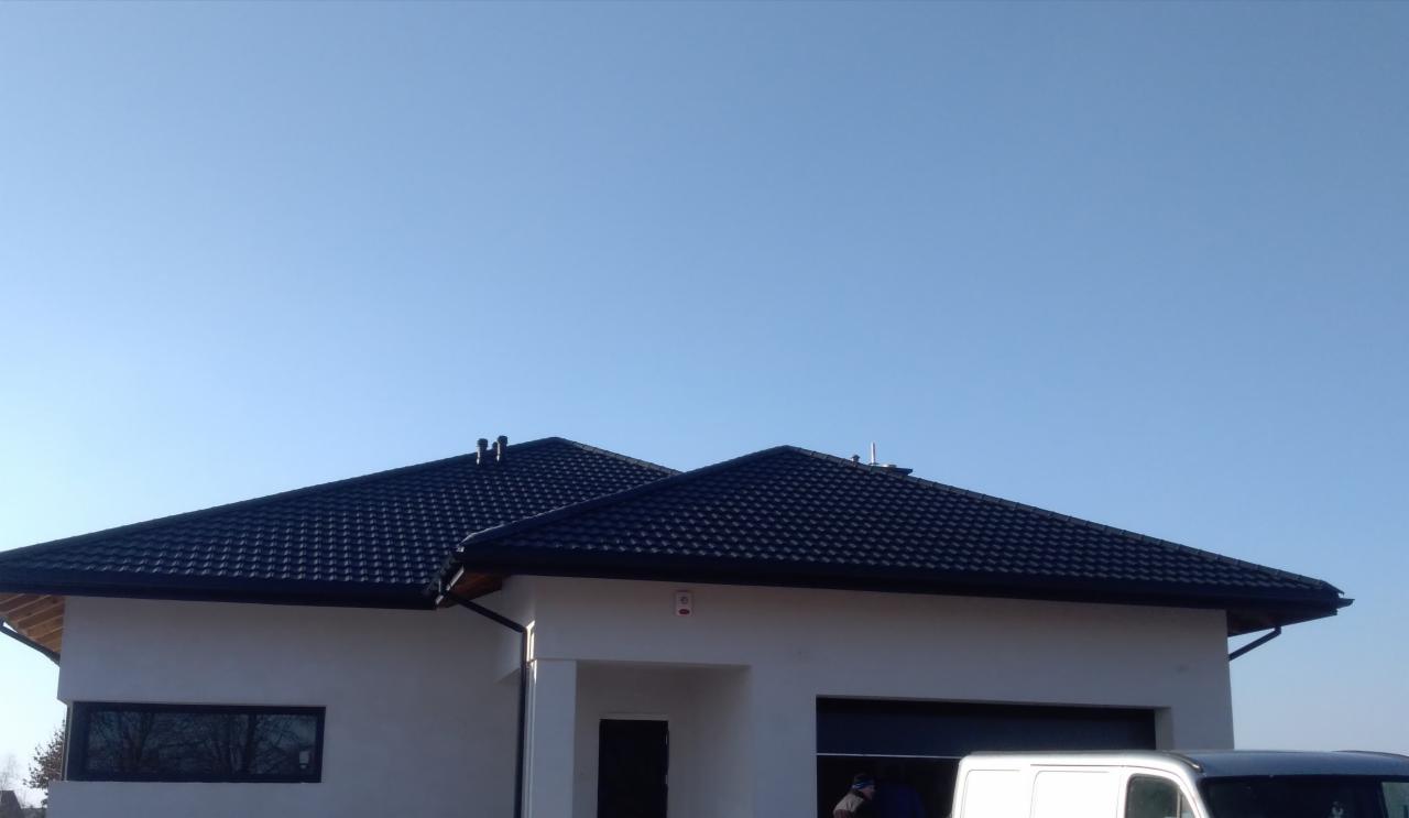 Nowoczesny dom jednorodzinny z ciemną dachówką modułową i orynnowaniem, zaparkowany biały bus w tle.