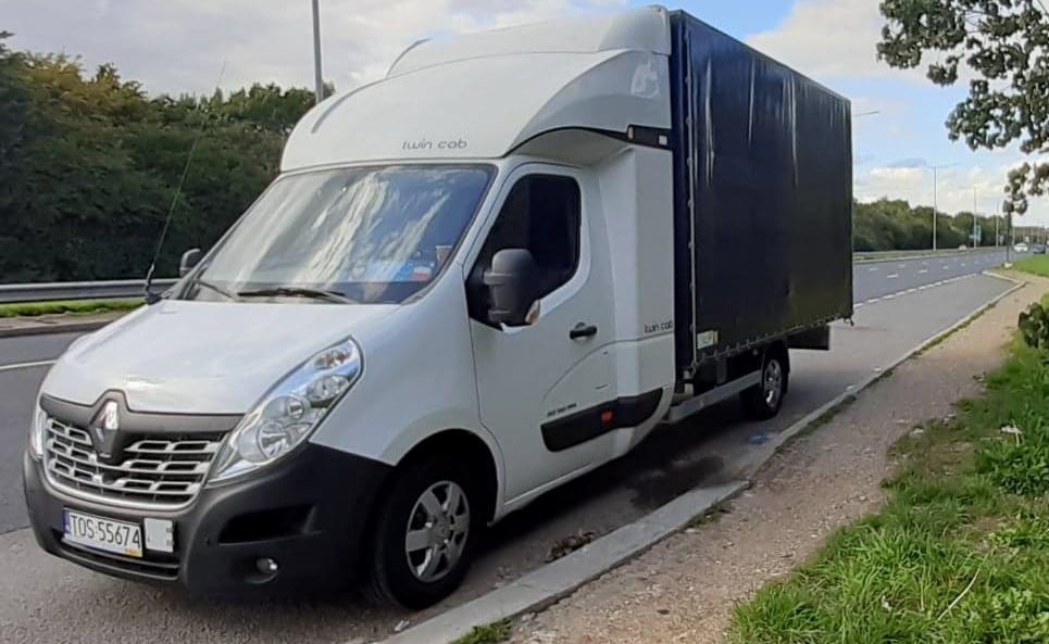 Biały samochód dostawczy Renault Master z zabudową plandekową typu Twin Cab zaparkowany przy drodze.