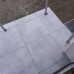 Świeżo ułożone, szare płytki gresowe na balkonie z widocznymi krzyżykami dystansowymi, otoczone metalowymi słupkami balustrady i widokiem na ziemię.