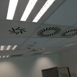 Sufit podwieszany w biurze z kratkami wentylacyjnymi o różnych wzorach i oświetleniem rastrowym.