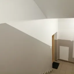 Klatka schodowa po malowaniu w Tarnawie, z szarą lamperią i białymi ścianami powyżej, widoczne piony gazowe w szafkach.