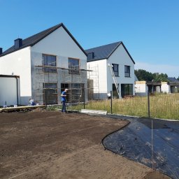 Proxential sp. z o.o. - Przygotowanie terenu pod ogród: wyrównana ziemia, rozłożona agrowłóknina, w tle nowe domy w trakcie wykończenia elewacji.