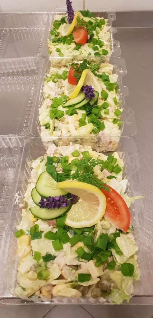 Trzy porcje sałatki jarzynowej w przezroczystych pojemnikach, udekorowane plasterkami cytryny, ogórka, pomidora, szczypiorkiem i gałązką lawendy.