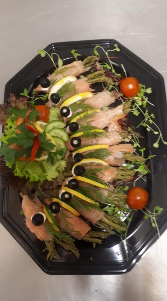 Dekoracyjna kompozycja z łososia, szparagów, cytryny i oliwek na czarnym, ośmiokątnym talerzu, przypominająca ryby, udekorowana sałatą i kiełkami.