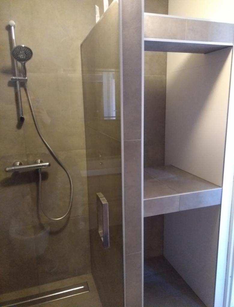 Nowoczesna kabina prysznicowa z szarymi płytkami, deszczownicą i wbudowaną półką wnękową.