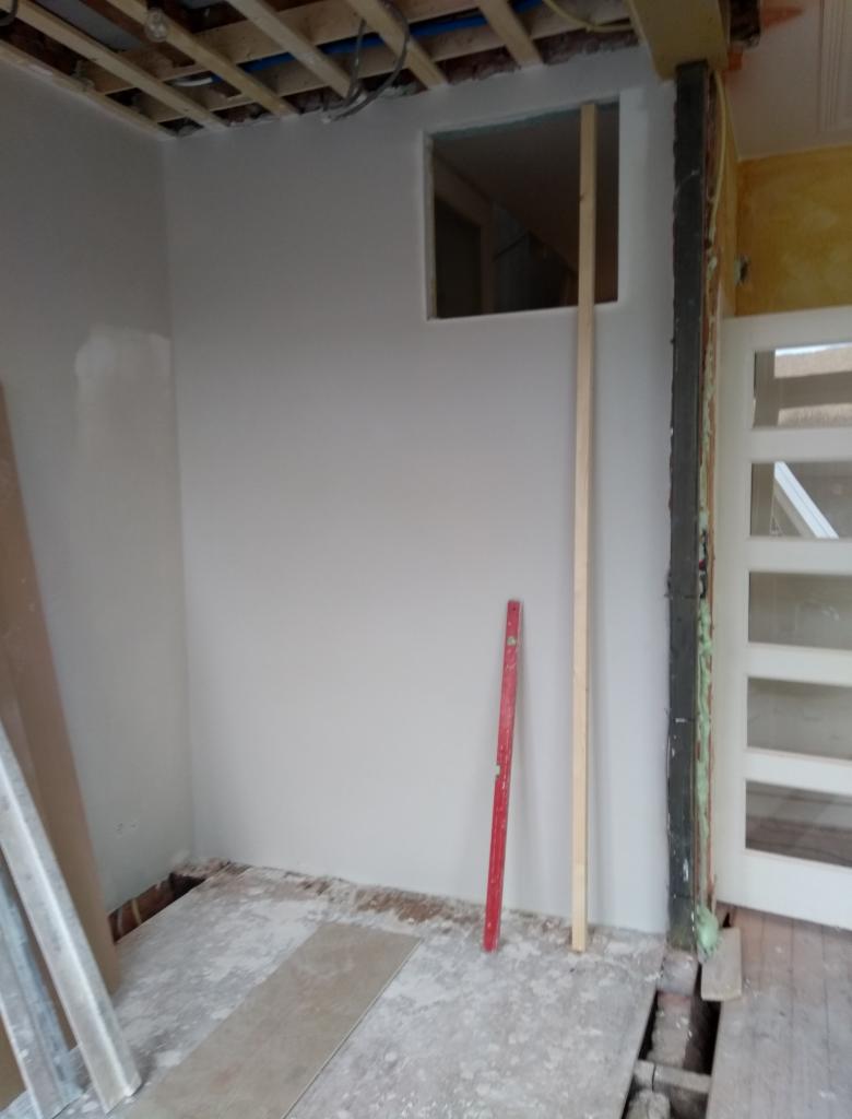 Wnętrze w trakcie remontu w Haarlem, widoczne otynkowane ściany z otworem okiennym, odsłonięty strop i podłoga w trakcie prac wykończeniowych, czerwona poziomica oparta o ścianę.