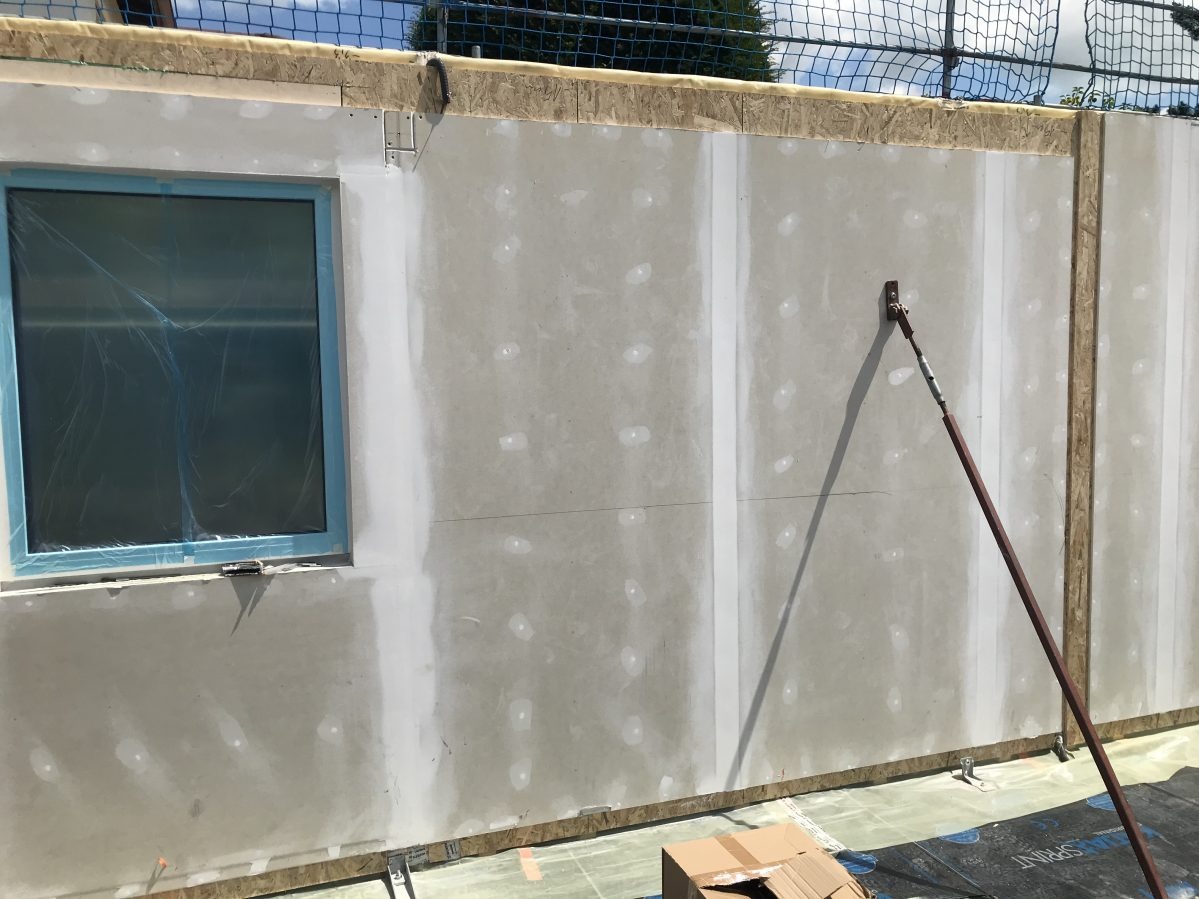 Wewnętrzna ściana w trakcie wykańczania, widoczne płyty gipsowo-kartonowe, okno zabezpieczone folią, podpora pionowa.