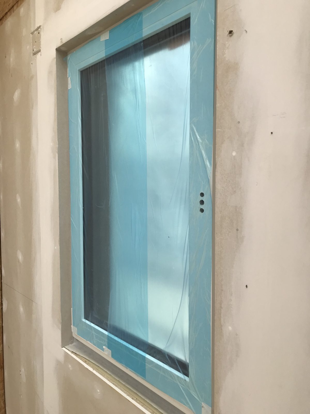 Nowe okno z niebieską folią ochronną w surowym wnętrzu, ściany przygotowane do malowania.
