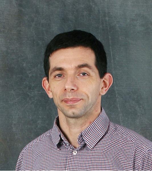 Portret mężczyzny w koszuli w drobną kratkę na szarym tle.