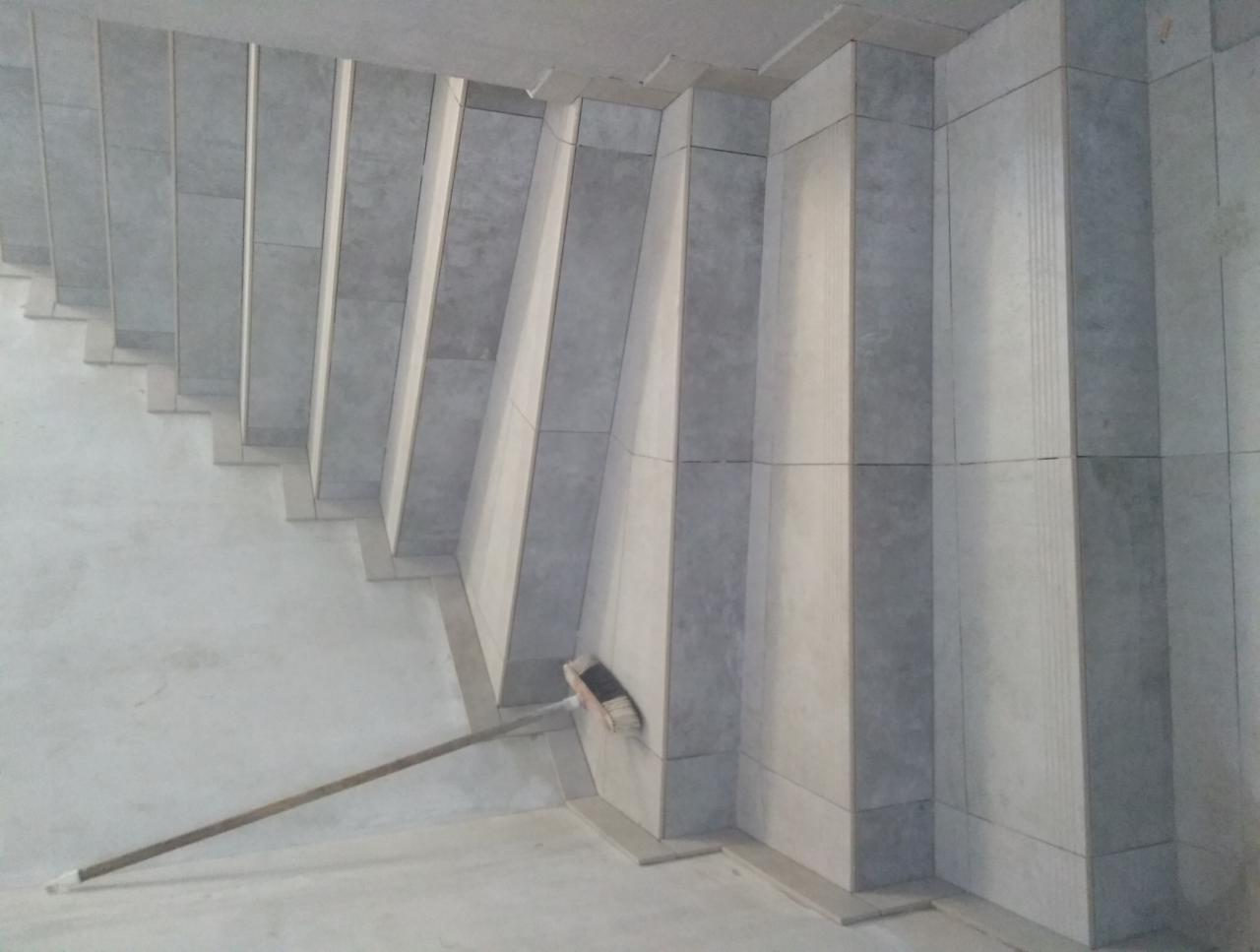 Klatka schodowa w Niwiskach wyłożona szarymi płytkami, widoczna szczotka oparta o ścianę, prace w toku.