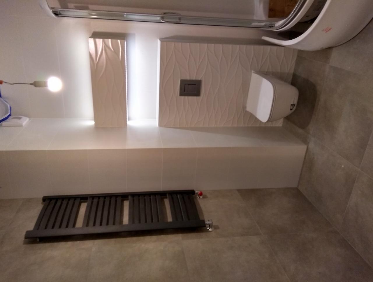 Nowoczesna łazienka z podwieszaną toaletą, grzejnikiem drabinkowym w kolorze antracytowym i dekoracyjnymi panelami ściennymi z subtelnym wzorem fal.