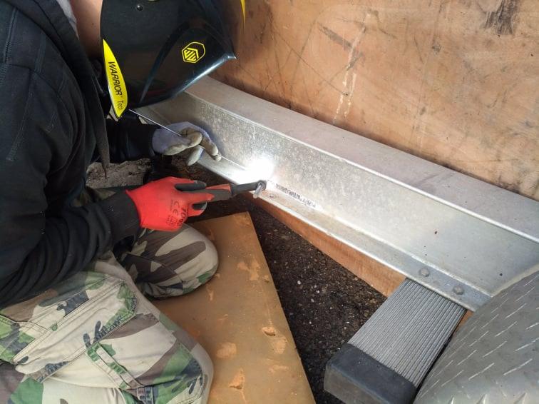 Proces łączenia metalu: spawanie elementu konstrukcyjnego z użyciem maski ochronnej i rękawic roboczych. Widoczne iskry i spaw.