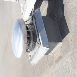 Metalowy wentylator dachowy z okrągłą osłoną i kratką, zamontowany na płaskim dachu z widocznymi uszczelnieniami i łatami.