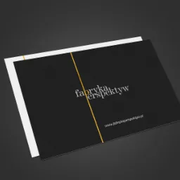 Elegancka wizytówka firmy z czarnym tłem, złotą linią i białym tekstem 'fabryka perspektyw' oraz adresem strony internetowej, leżąca na ciemnoszarym tle pod kątem.