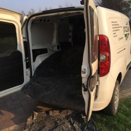 Pro-Clean s.c - Otwarty bagażnik białego samochodu dostawczego wypełniony workiem z czarną folią zawierającym resztki roślinne, zaparkowanego na trawniku przed posesją.