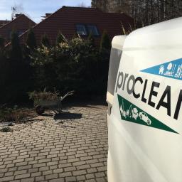 Pro-Clean s.c - Furgonetka z logo firmy Proclean na tle posesji z przyciętymi gałęziami i taczką, sugerująca prace porządkowe na zewnątrz.
