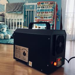 Pro-Clean s.c - Czarny generator ozonu marki Korona na drewnianej podłodze w pokoju dziecięcym, z widocznym łóżeczkiem, pluszowym misiem i zasłonami w tle.