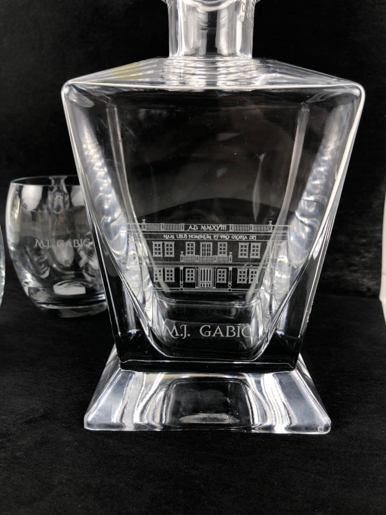 Karafka i szklanka z grawerowanym motywem architektonicznym i napisem 'M.J. Gabic' na czarnym tle.
