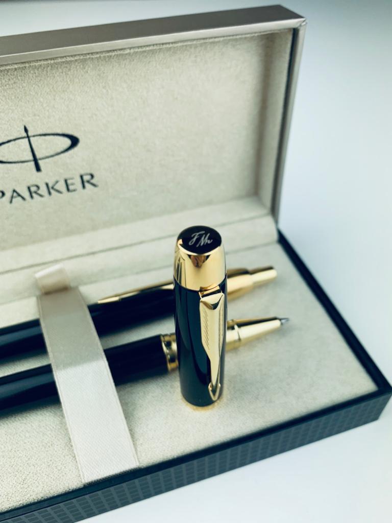 Zestaw piśmienniczy Parker w eleganckim pudełku prezentowym z kremową wstążką, widoczny długopis z wygrawerowanymi inicjałami 'JM' na skuwce.