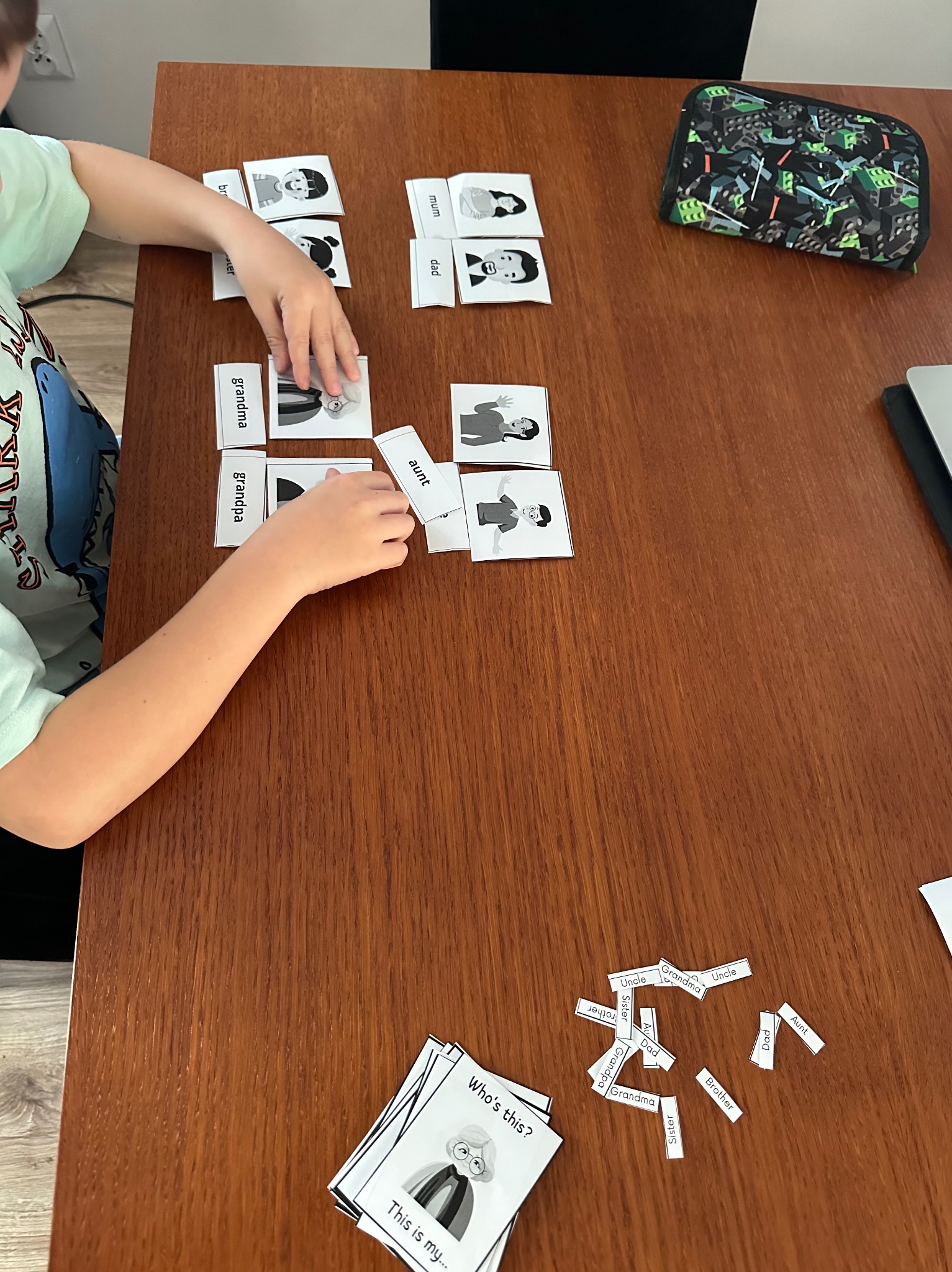 Chłopiec układa karty z wizerunkami członków rodziny i podpisami na drewnianym stole. Nauka słownictwa angielskiego w formie zabawy.