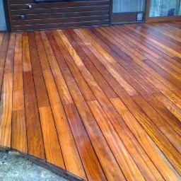 Błyszczący, świeżo polakierowany taras z egzotycznego drewna, widok z góry, z fragmentem surowego gruntu przy krawędzi