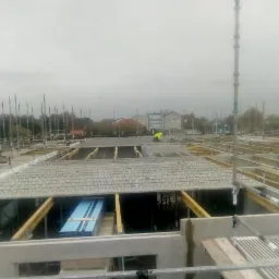 Wiązanie zbrojenia stropu na budowie domu murowanego, widoczny pracownik w odblaskowej kamizelce i niebieskie płyty izolacyjne.