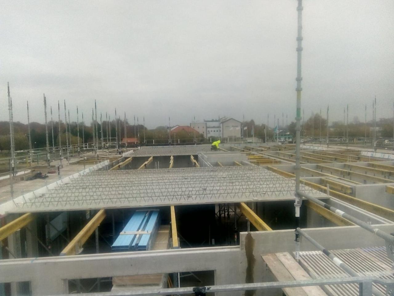 Wiązanie zbrojenia stropu na budowie domu murowanego, widoczny pracownik w odblaskowej kamizelce i niebieskie płyty izolacyjne.