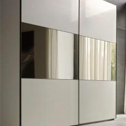 Meb-Le - Nowoczesna szafa przesuwna z białymi panelami i lustrzanymi wstawkami, odbijająca zasłony i fragment okna.