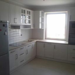 Meb-Le - Jasna, funkcjonalna kuchnia z białymi frontami szafek, płytą indukcyjną i wbudowanym piekarnikiem, oświetlona naturalnym światłem z okna.