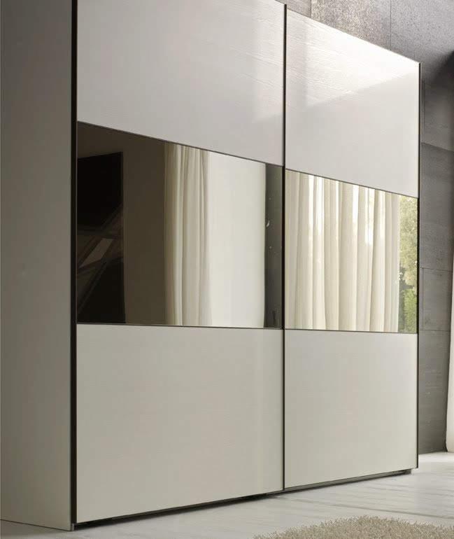 Nowoczesna szafa przesuwna z białymi panelami i lustrzanymi wstawkami, odbijająca zasłony i fragment okna.