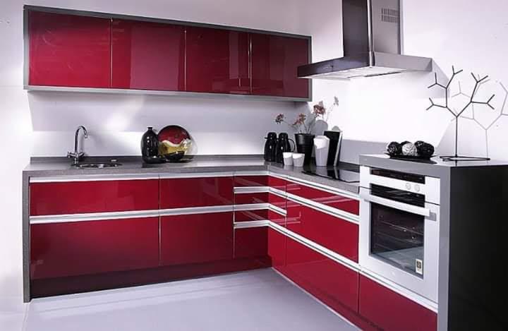 Nowoczesna kuchnia z błyszczącymi, bordowymi frontami szafek, szarym blatem i białymi ścianami, uzupełniona o srebrny okap i dekoracyjne akcesoria.