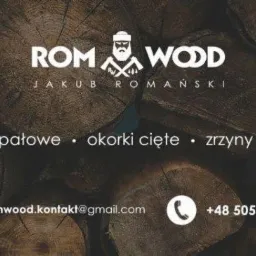 Grafika reklamowa firmy ROM-WOOD Jakub Romański z Pogórza, oferującej drewno opałowe, okorki cięte i zrzyny tartaczne, na tle stosu drewna. Widoczne logo firmy z wizerunkiem drwala i skrzyżowanymi...