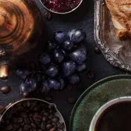 Kompozycja z kawą, dżemem, croissantem i winogronami na ciemnym tle, z elementami w stylu vintage.
