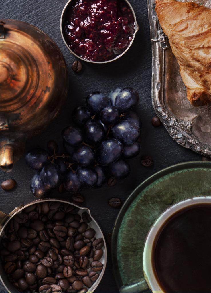 Kompozycja z kawą, dżemem, croissantem i winogronami na ciemnym tle, z elementami w stylu vintage.