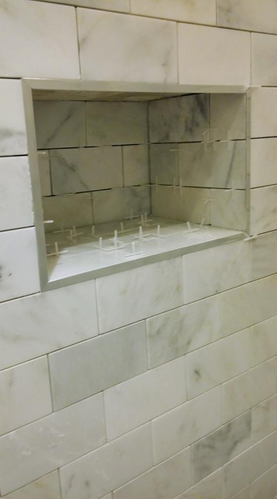 Wnęka w ścianie wyłożonej marmurowymi płytkami, z widocznymi krzyżykami dystansowymi, gotowa do fugowania.