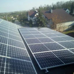 Instalacja fotowoltaiczna na dachu domu jednorodzinnego, widok z góry na panele słoneczne w regularnym układzie, w tle zabudowa mieszkalna i drzewa.