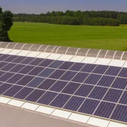 Instalacja paneli słonecznych na dachu budynku w Kielcach, z widocznymi świetlikami dachowymi i zielonym krajobrazem w tle.