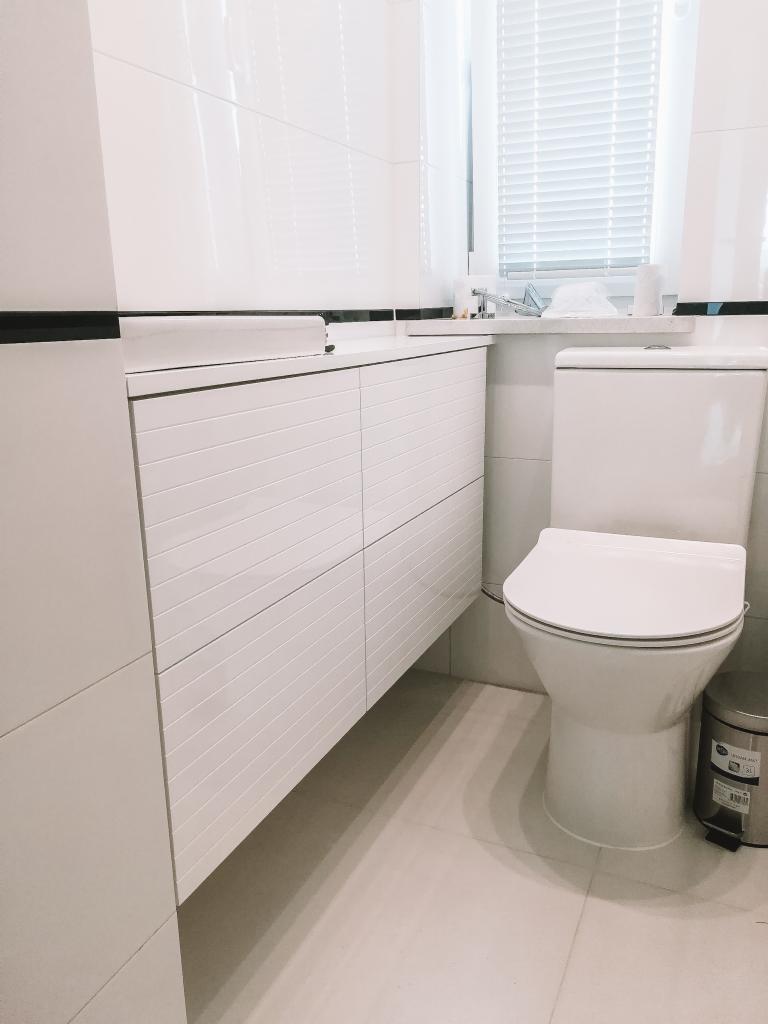 Biała łazienka z wiszącą szafką pod umywalką z poziomymi frezowaniami, toaletą i koszem na śmieci z metalu.