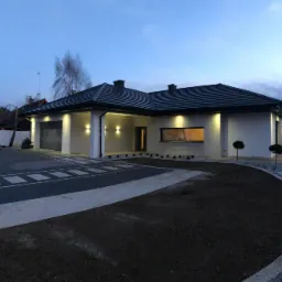 Nowoczesny dom jednorodzinny z oświetleniem zewnętrznym w Tarnowie, widok z podjazdu o zmierzchu.